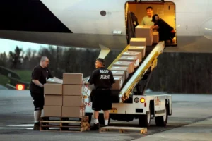Airport cargo workers placing packages on a conveyor belt leading to an airplane.