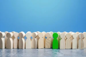 Green wooden figure standing out among plain wooden figures