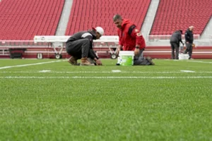 Grounds maintenance workers checking the field lines on a football field.