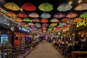Outdoor marketplace with restaurants and colorful umbrellas suspended overhead.