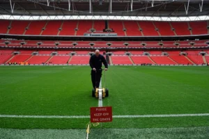 Sports field maintenance worker painting boundary lines on a football pitch.