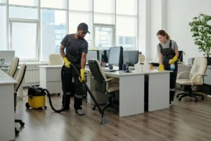 Two cleaning staff cleaning an office workspace.