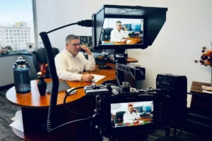 Businessman talking on the phone while being filmed in an office.