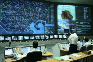 People monitoring Geographic Information System (GIS) maps on a large display screen.