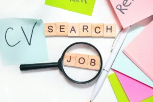 Magnifying glass highlighting the word "Job" beside a notepad labeled "CV" and a pen.