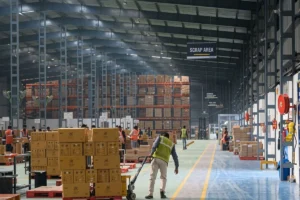 Worker transporting boxes using a manual pallet jack in a warehouse.